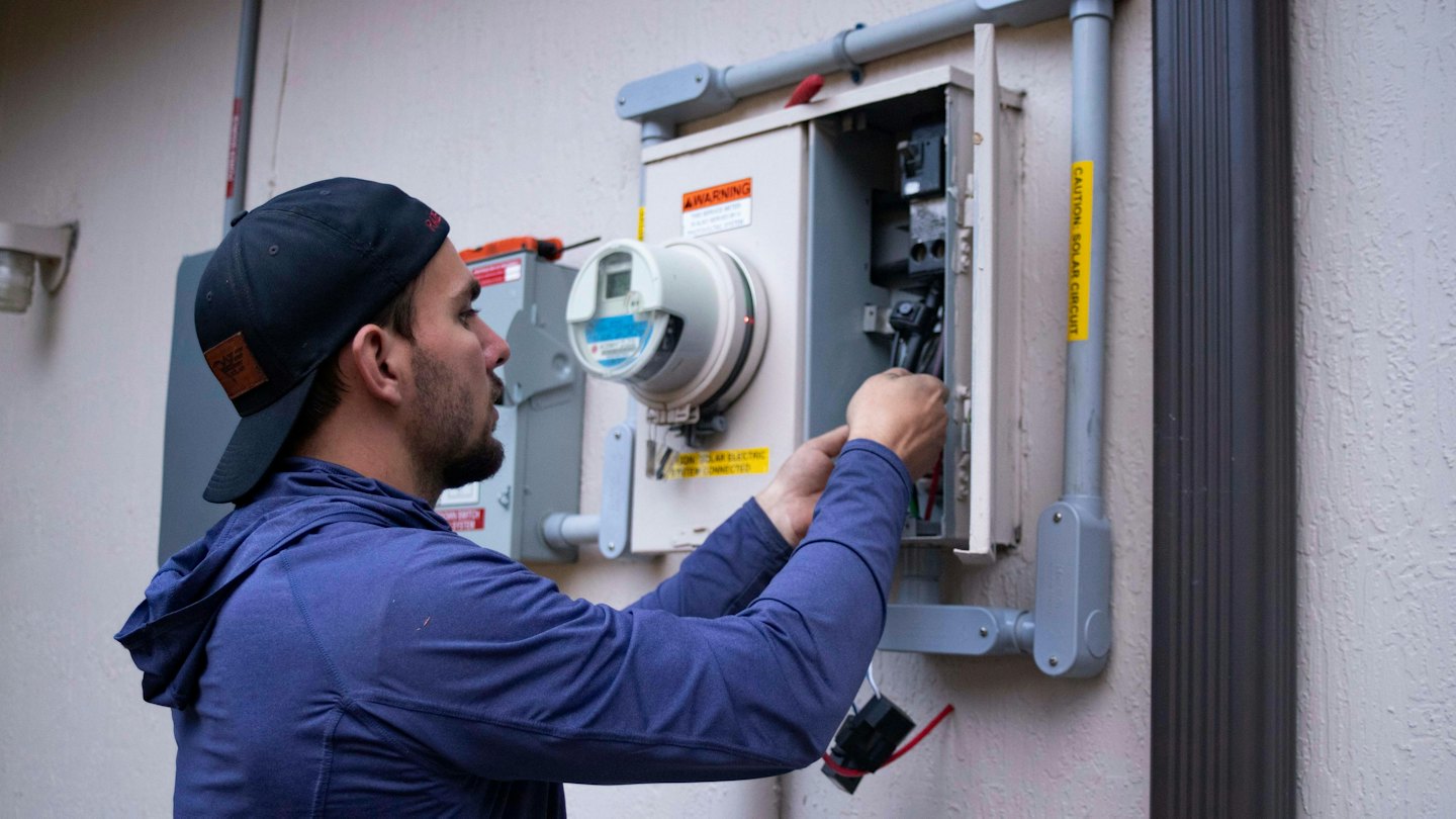 Técnico conectando cables en un panel eléctrico exterior.